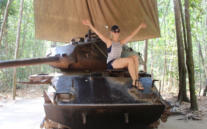 Person sitting on a tank at Cu Chi Tunnels, Vietnam, surrounded by forest.