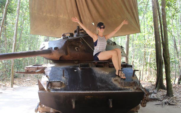 Person sitting on a tank at Cu Chi Tunnels, Vietnam, surrounded by forest.