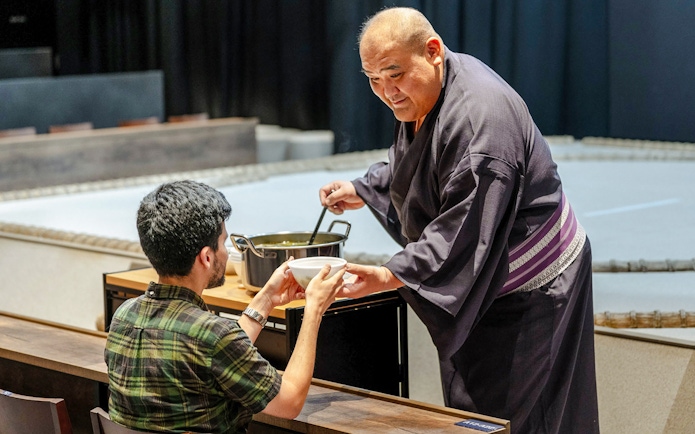 Sumo wrestler serving soup to a guest at The Sumo Hall Hirakuza Osaka.