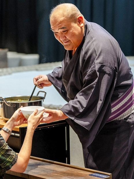 Sumo wrestler serving soup to a guest at The Sumo Hall Hirakuza Osaka.