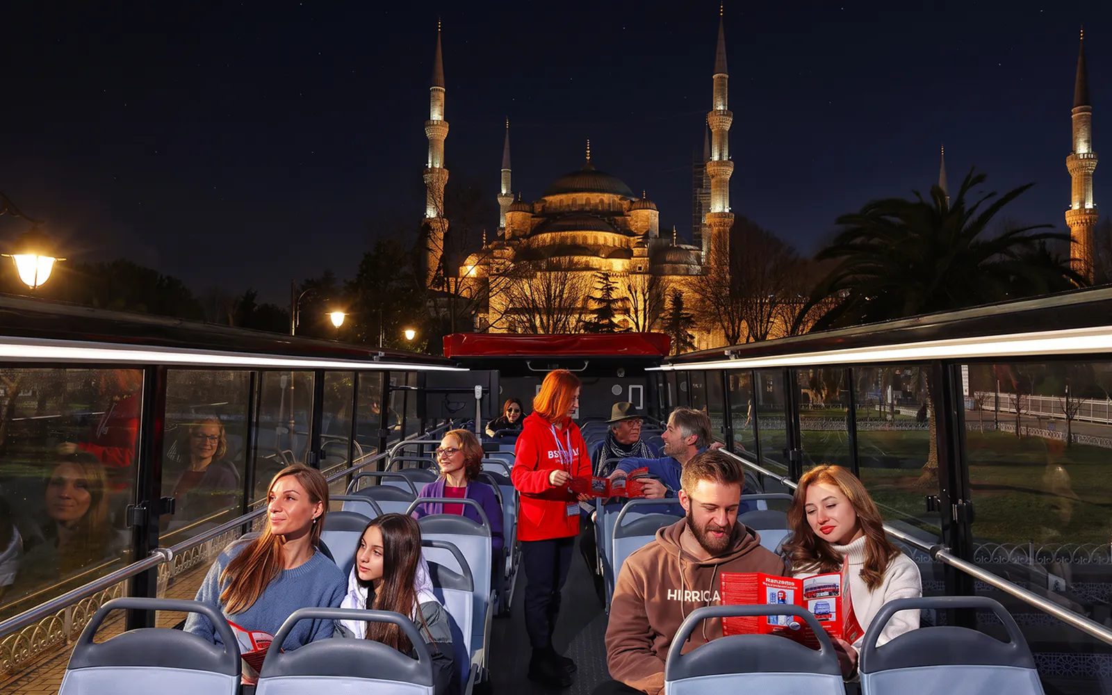 Open-top bus tour in Istanbul with view of illuminated Blue Mosque at night.