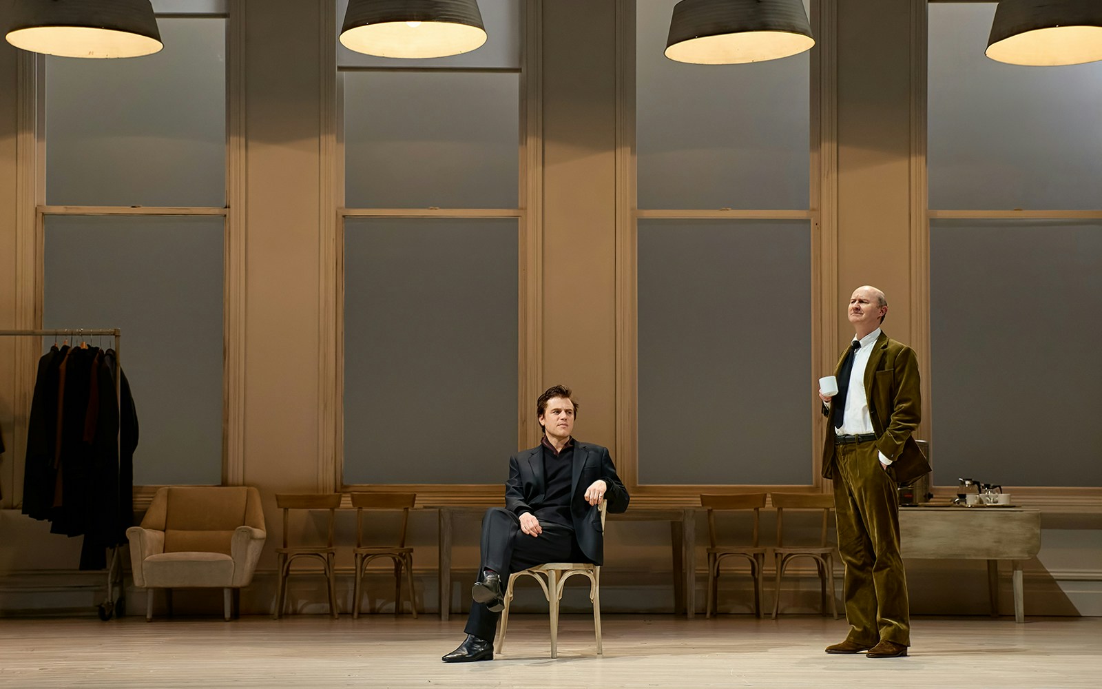 Two actors on stage during "The Motive and the Cue" performance, one seated, one standing with a cup.