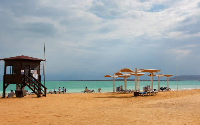 Dead Sea resort beach with lifeguard tower and sunshades by the water.