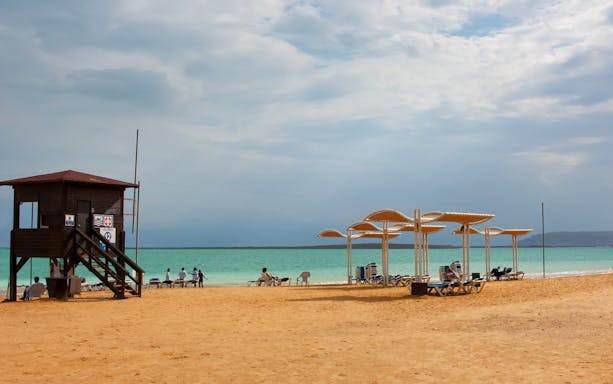 Dead Sea resort beach with lifeguard tower and sunshades by the water.