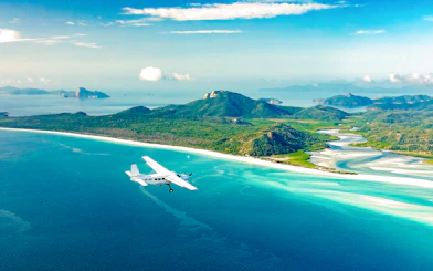 Aerial view of Whitsundays with a plane flying over turquoise waters and lush islands, Australia.