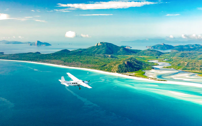 Aerial view of Whitsundays with a plane flying over turquoise waters and lush islands, Australia.