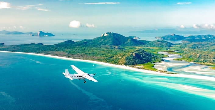 Aerial view of Whitsundays with a plane flying over turquoise waters and lush islands, Australia.