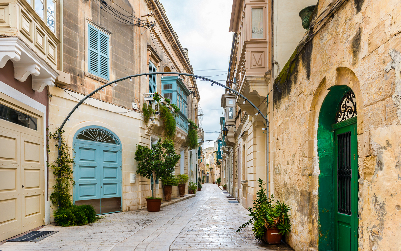 Narrow street in Rabat, Malta with traditional limestone buildings and colorful balconies.