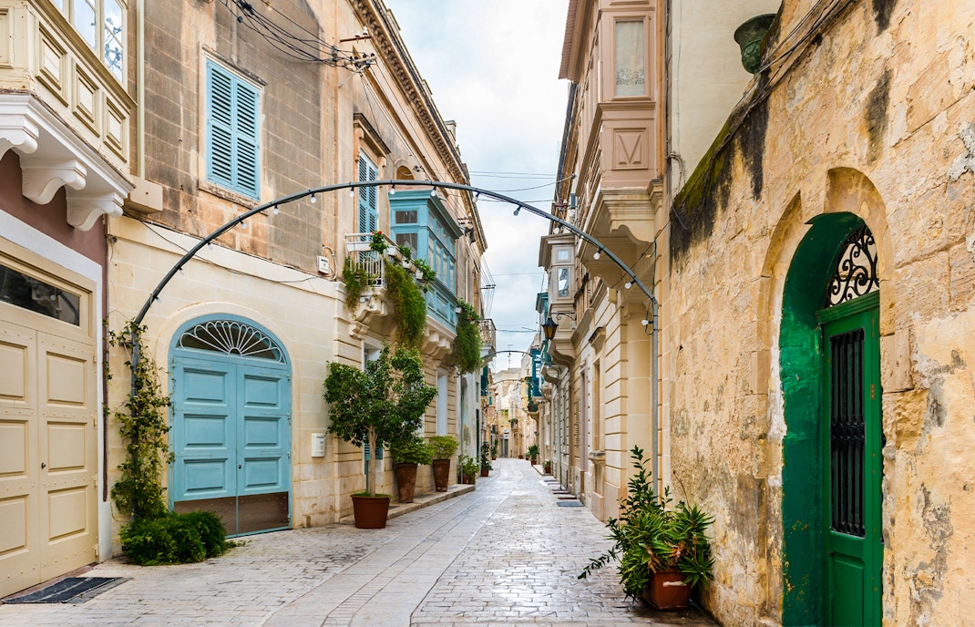 Narrow street in Rabat, Malta with traditional limestone buildings and colorful balconies.