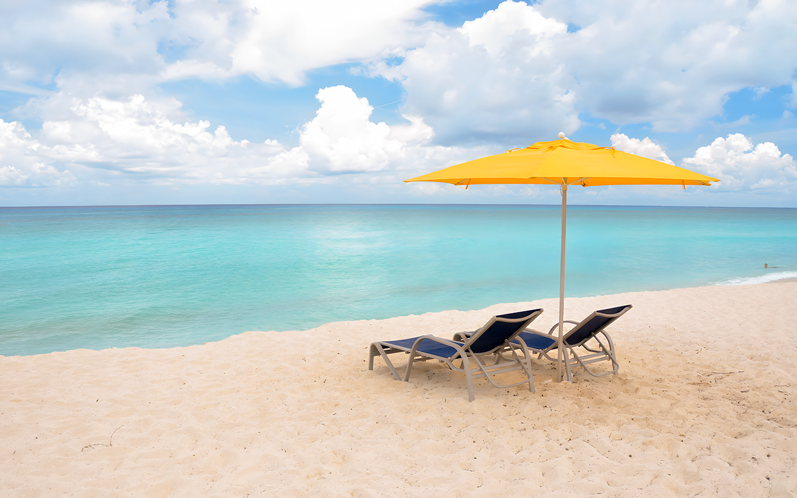 Two lounge chairs under a yellow umbrella on a sandy beach in Bimini, Bahamas.