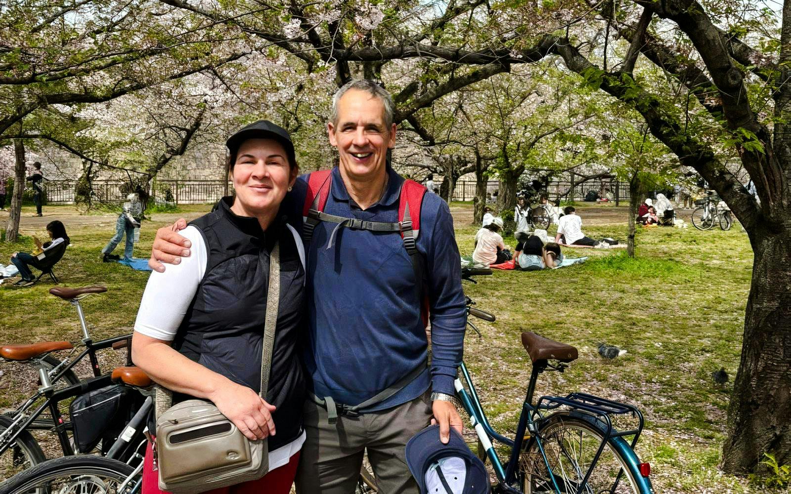Couple with bikes under cherry blossoms at Osaka Castle park.