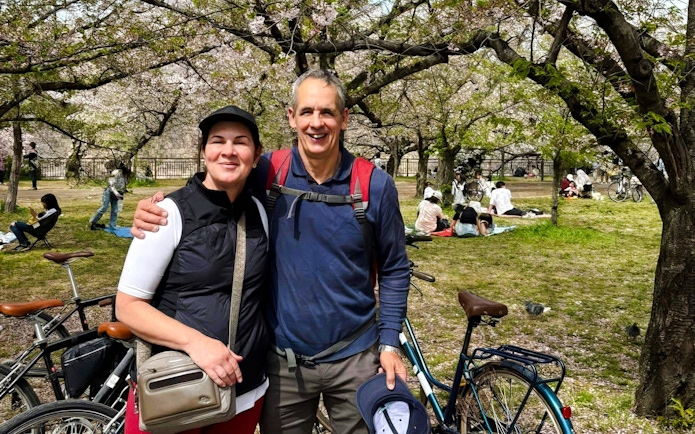 Couple with bikes under cherry blossoms at Osaka Castle park.