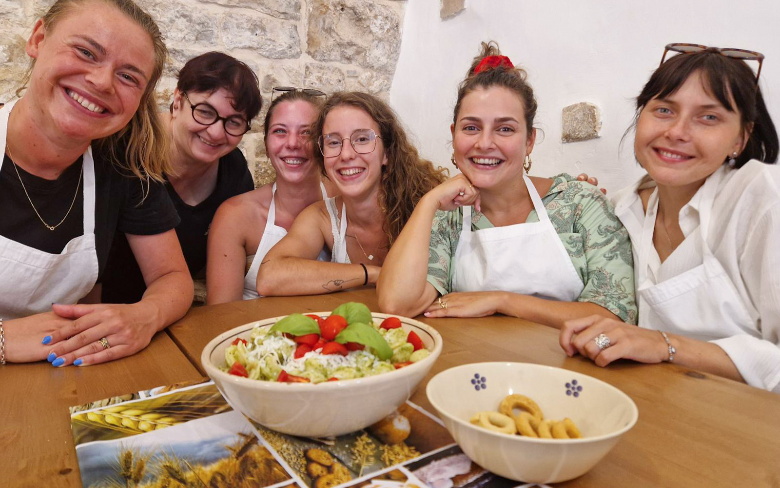 Women enjoying a cooking class in Polignano a Mare with fresh salad and snacks on the table.