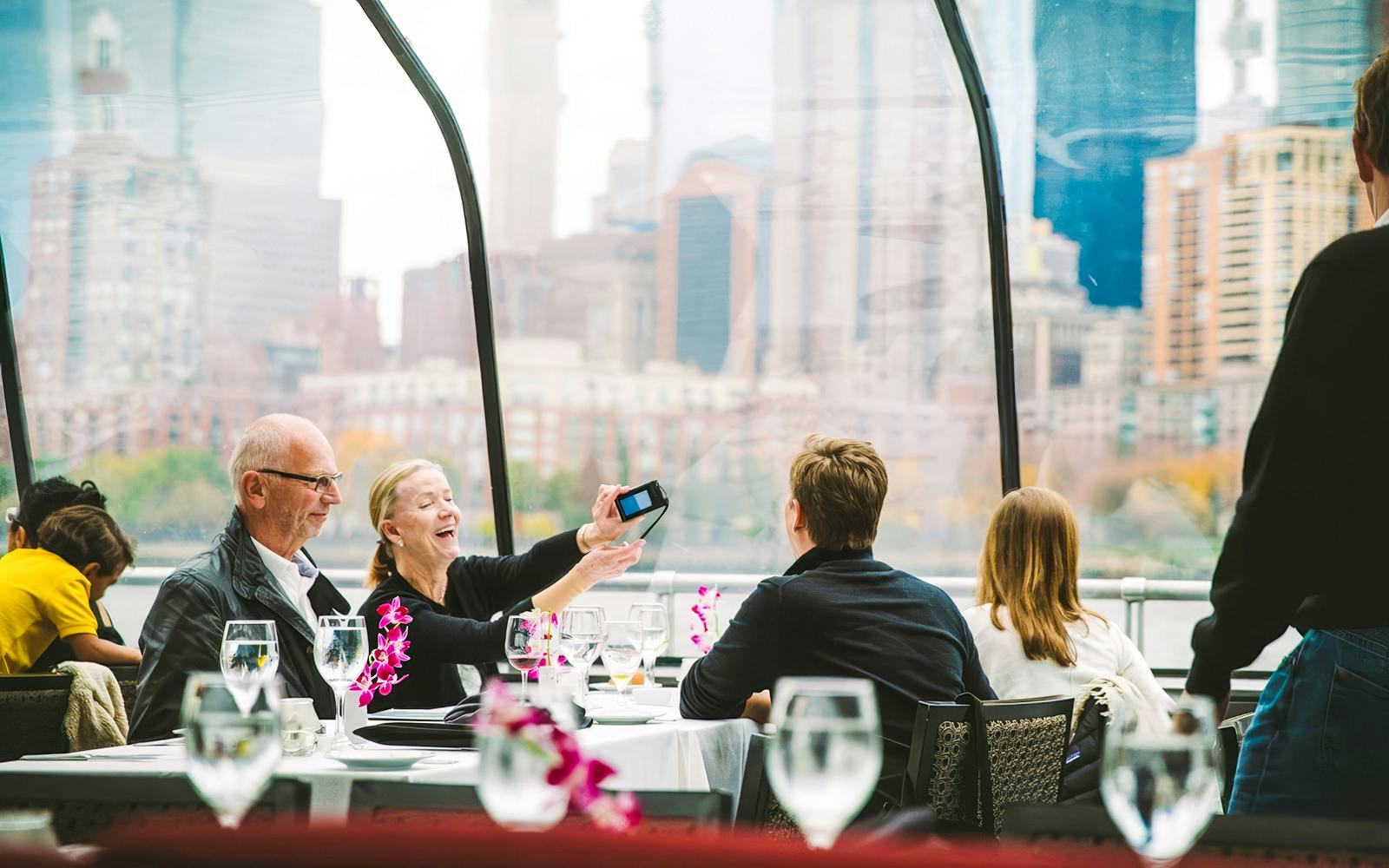 Guests enjoying brunch on a luxury glass boat cruise with city skyline views.