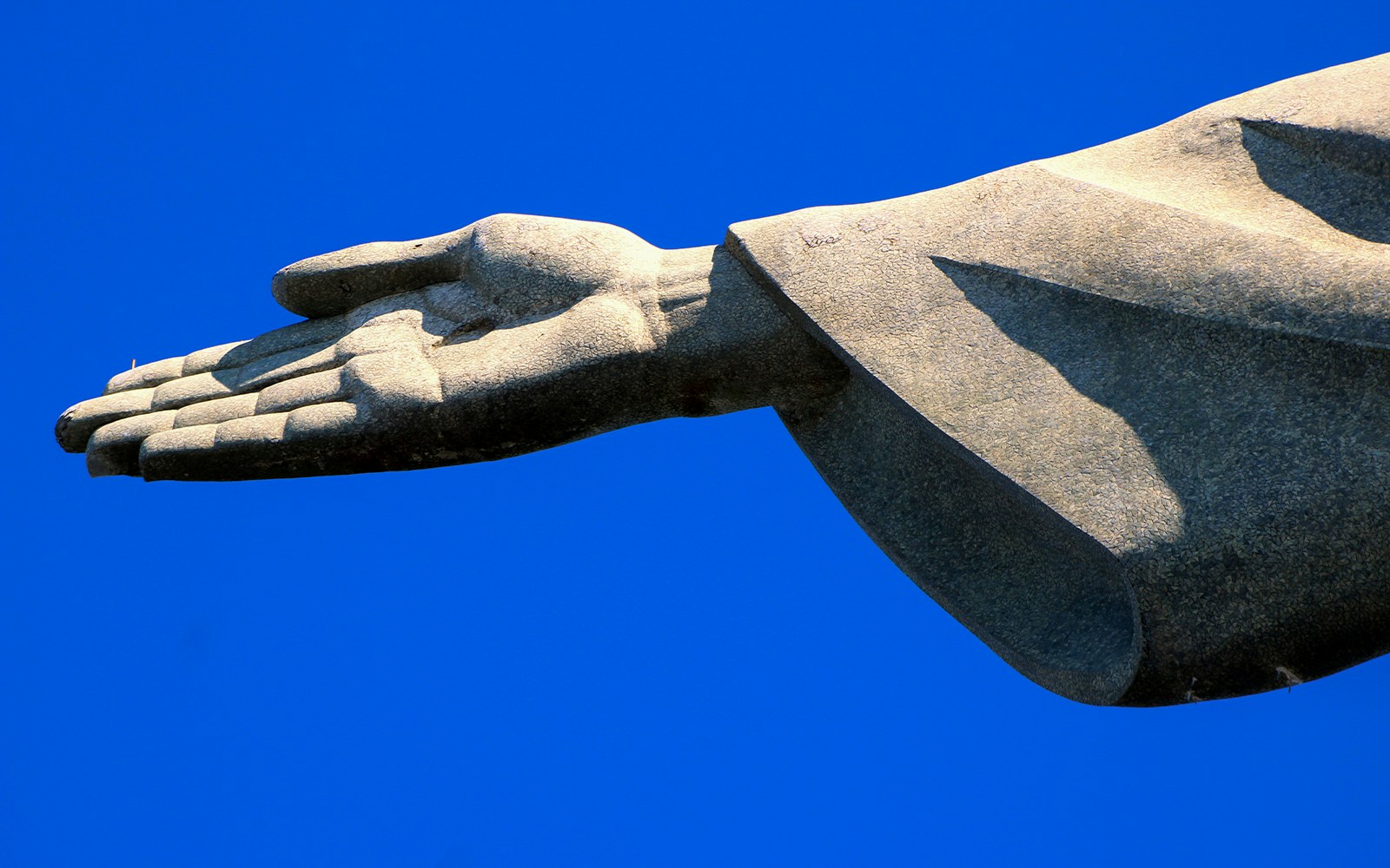 Christ the Redeemer statue hand detail against blue sky, Rio de Janeiro.