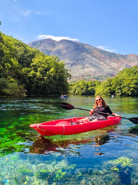 Kayaking on clear waters at The Blue Eye, Albania with lush greenery and mountains in the background.
