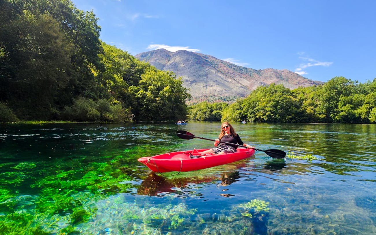 Kayaking on clear waters at The Blue Eye, Albania with lush greenery and mountains in the background.