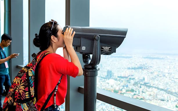 Visitor using telescope at Saigon Skydeck overlooking Ho Chi Minh City.