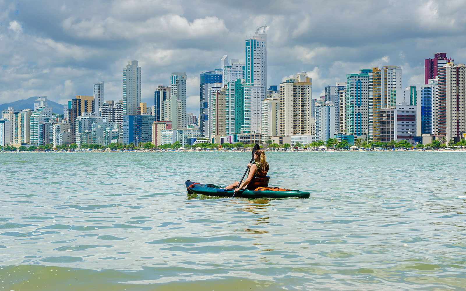 Kayaker paddling on Dubai Creek with city skyline in the background.