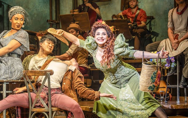 Performers in a theatrical scene, one in a green dress holding a basket, related to ghost stories.