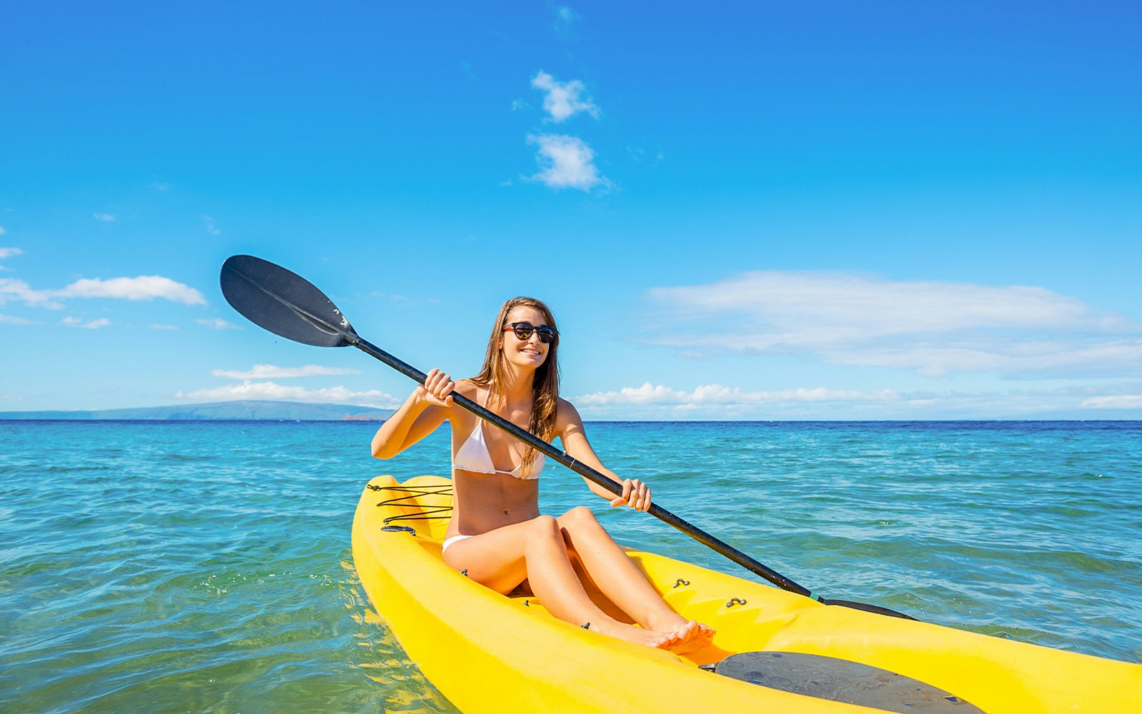 Woman kayaking on a yellow kayak in the ocean under a clear blue sky.