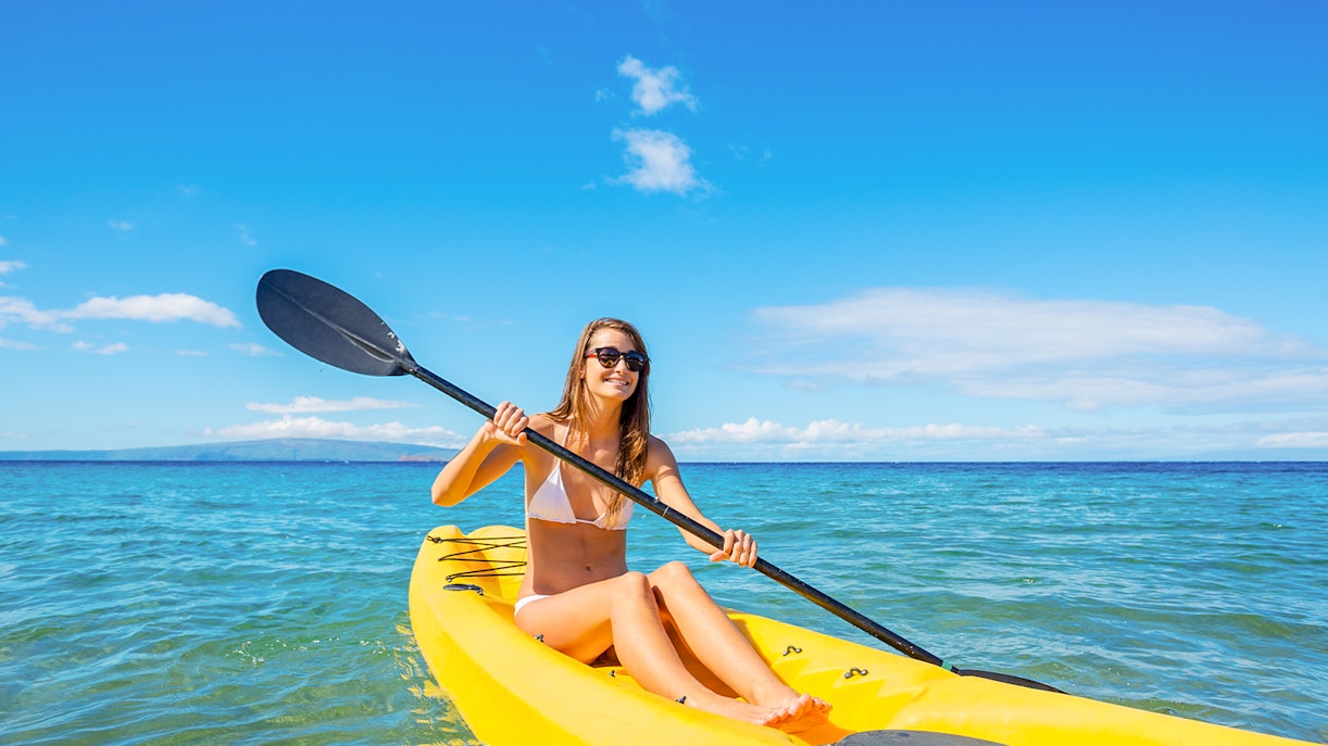 Woman kayaking on a yellow kayak in the ocean under a clear blue sky.
