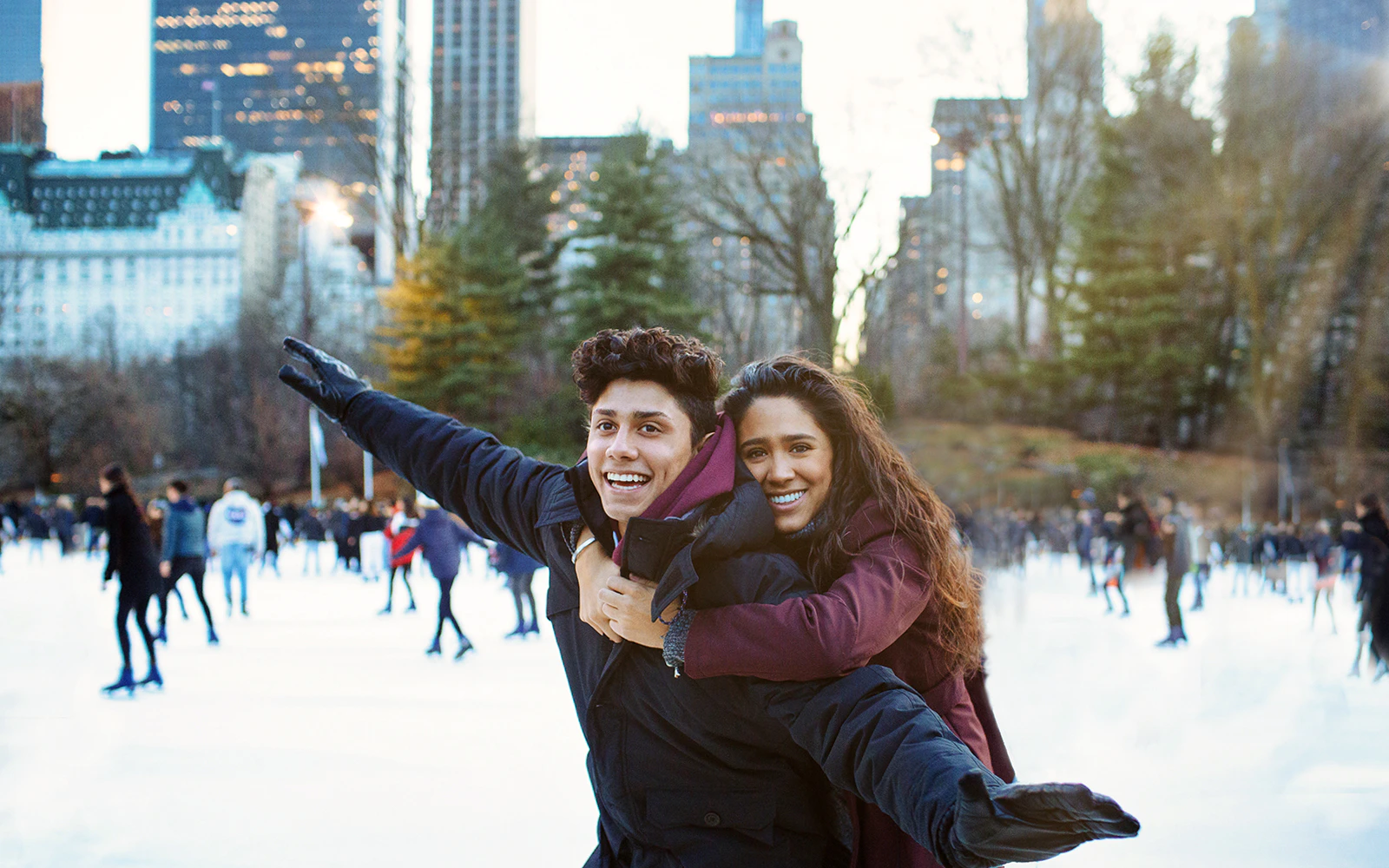 Couple enjoying ice skating in Central Park, New York City with skyline in background.