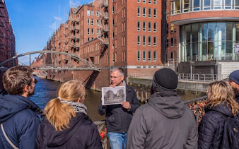 Guided tour group at Speicherstadt, Hamburg, with guide holding historical photo.