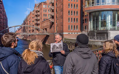 Guided tour group at Speicherstadt, Hamburg, with guide holding historical photo.
