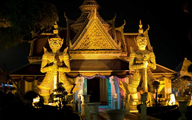 Giant guardian statues at Wat Arun temple illuminated at night, Bangkok Night Bike Tour.