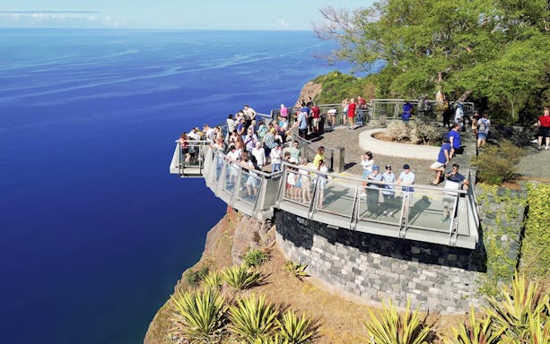 Visitors on Cabo Girão skywalk overlooking ocean, part of guided tour with transfers.