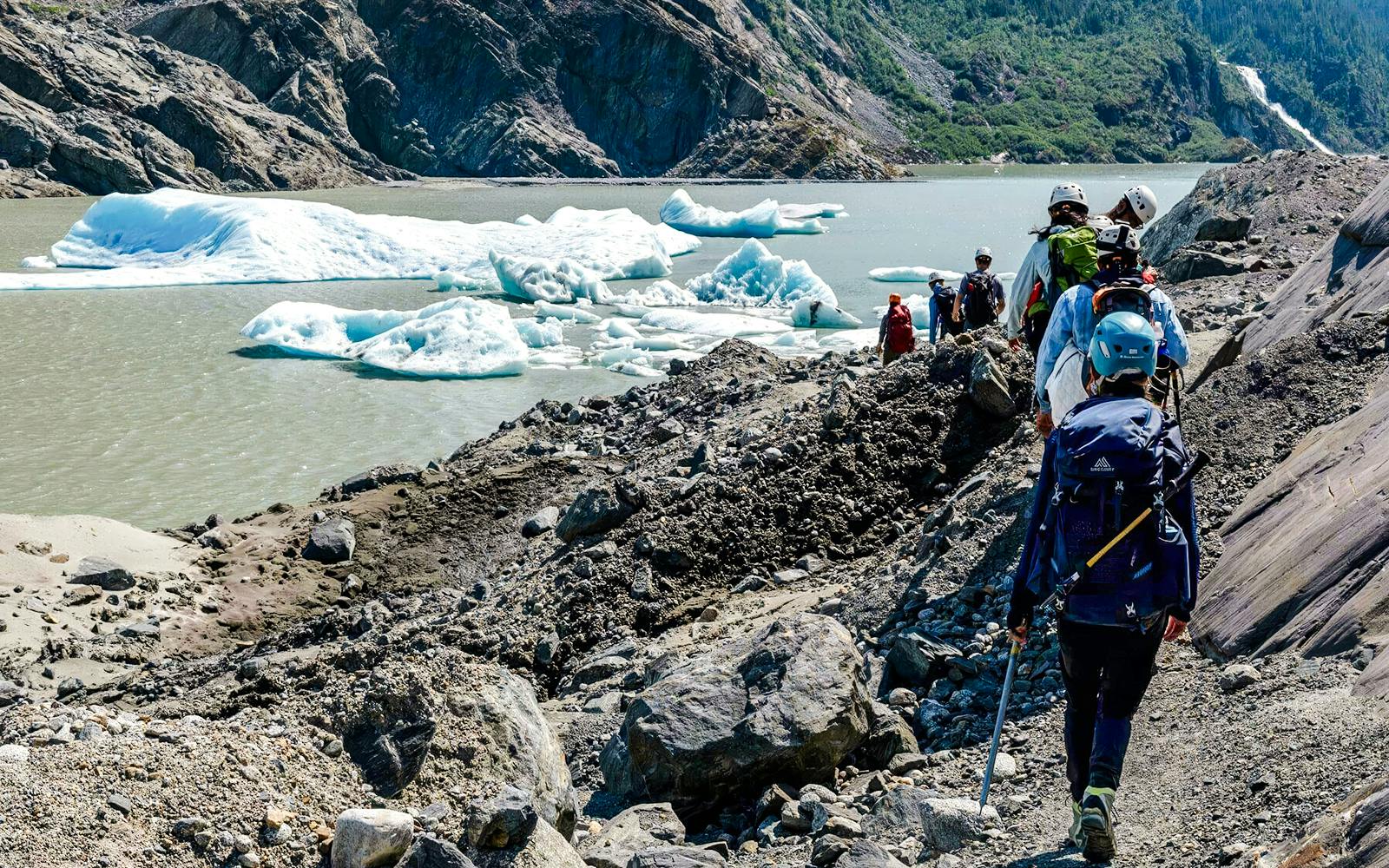 Hikers trekking along rocky terrain near Mendenhall Glacier, Alaska.