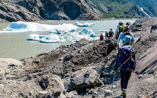Hikers trekking along rocky terrain near Mendenhall Glacier, Alaska.