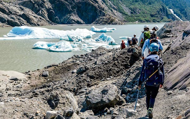 Hikers trekking along rocky terrain near Mendenhall Glacier, Alaska.