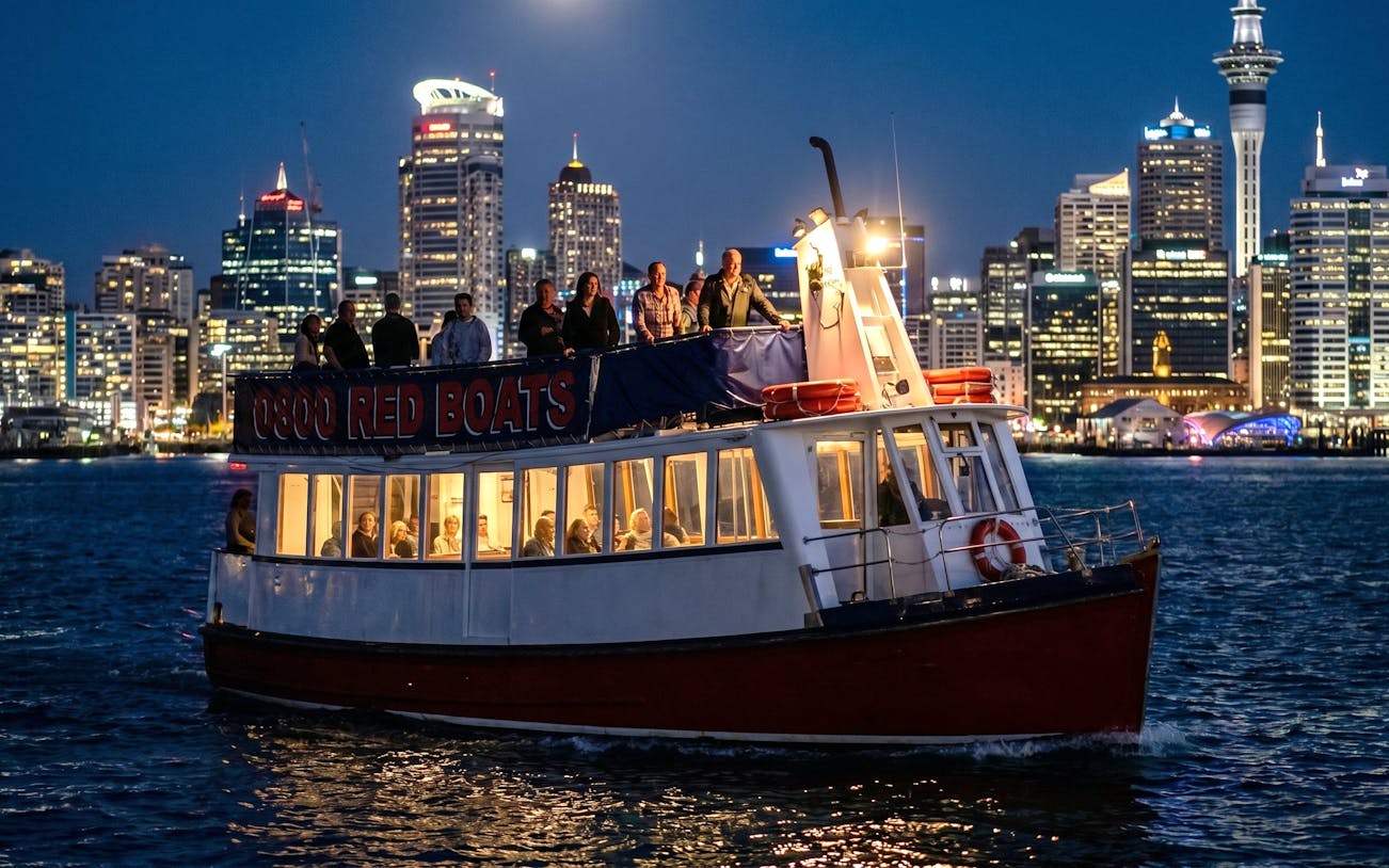 Auckland harbour cruise boat with passengers, city skyline illuminated at night.