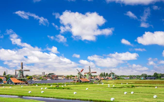 Windmills at Zaanse Schans with green fields and blue sky in the Netherlands.