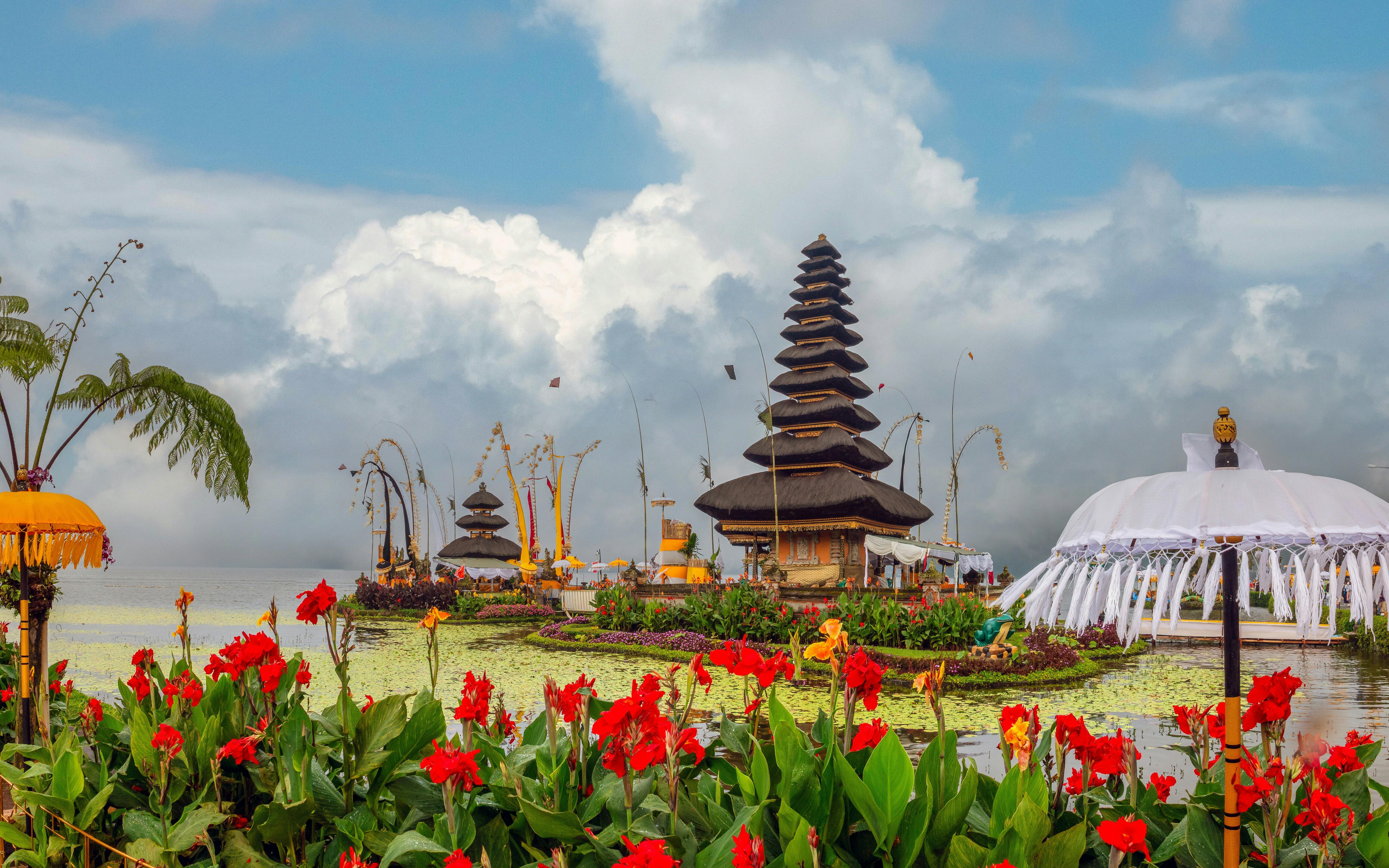 Ulun Danu temple complex on Beratan Lake with red flowers, Bali, Indonesia.
