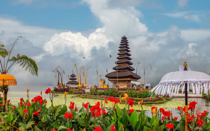 Ulun Danu temple complex on Beratan Lake with red flowers, Bali, Indonesia.