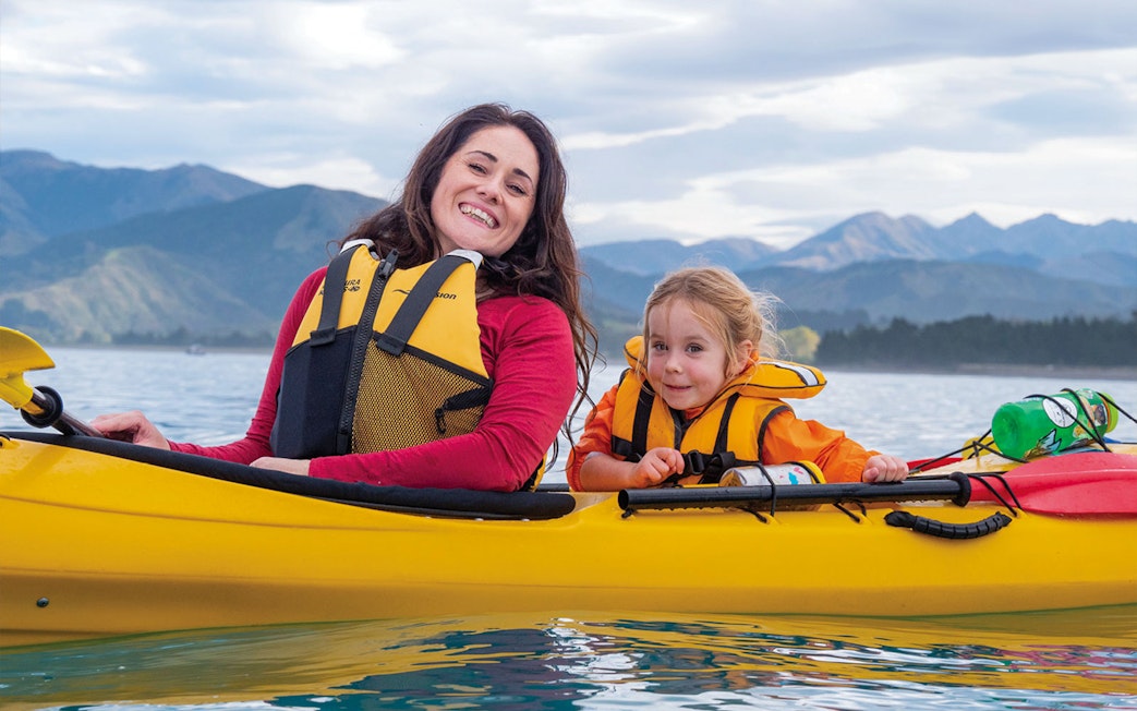 Mother and child kayaking on a lake with mountains in the background.