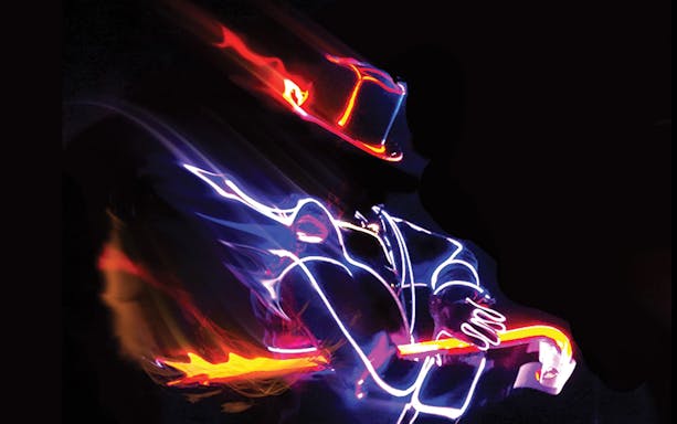 Performer in illuminated costume playing guitar at iLuminate show.