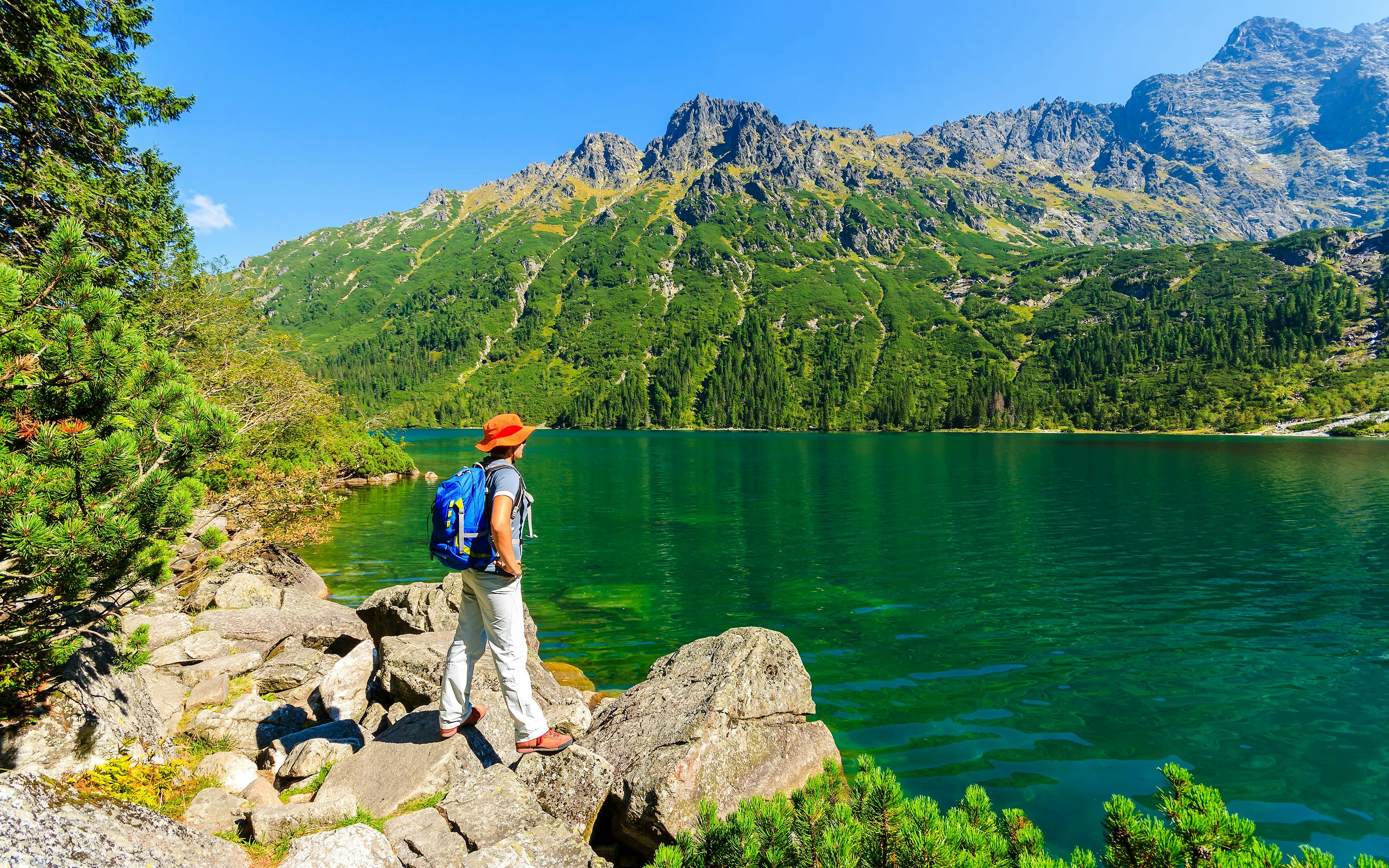 Woman tourist with backpack at Morskie Oko lake, Poland, admiring mountain view.