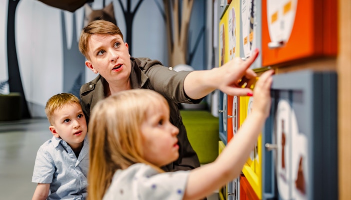 Mother and two children engaging in discovery games at an interactive natural history museum exhibition.