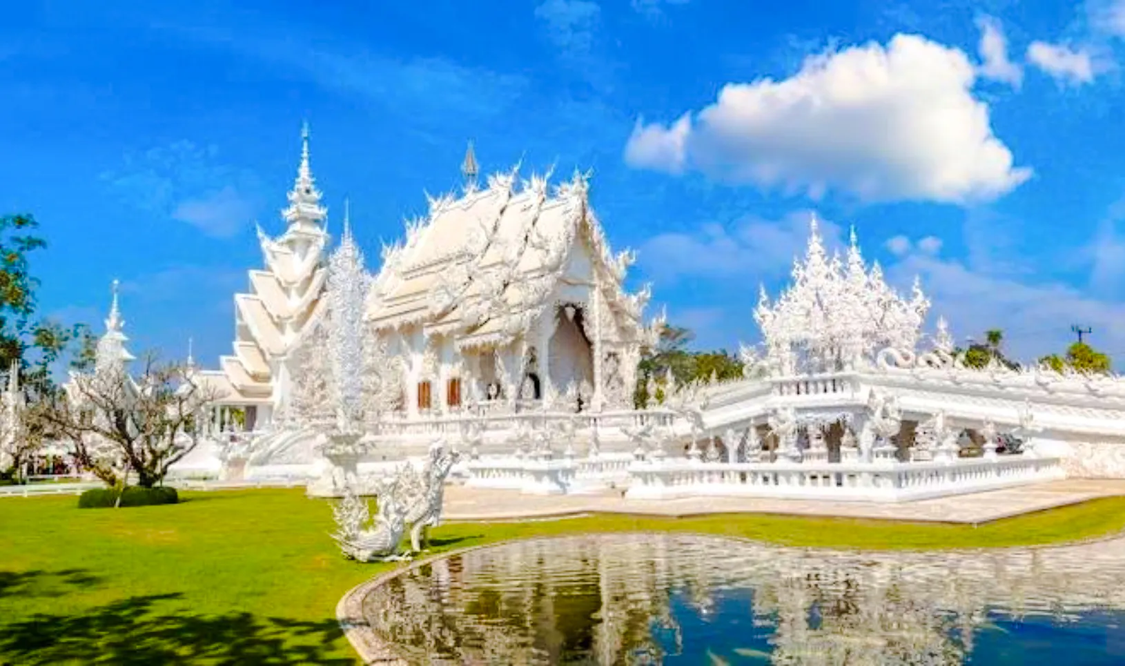 White Temple in Chiang Rai with intricate architecture and reflection in pond.