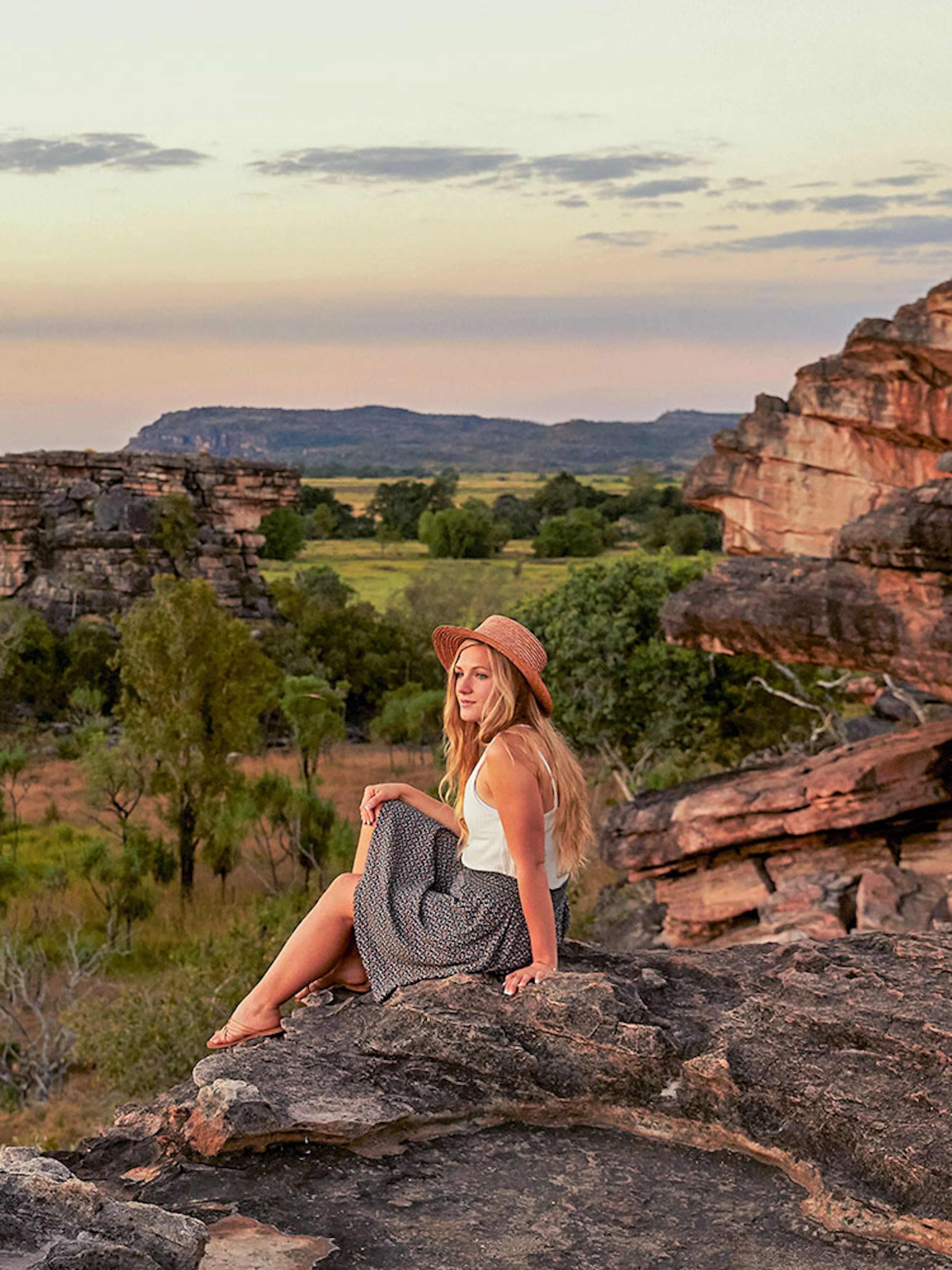 Woman sitting at Ubirr lookout with view of Kakadu National Park, Australia.