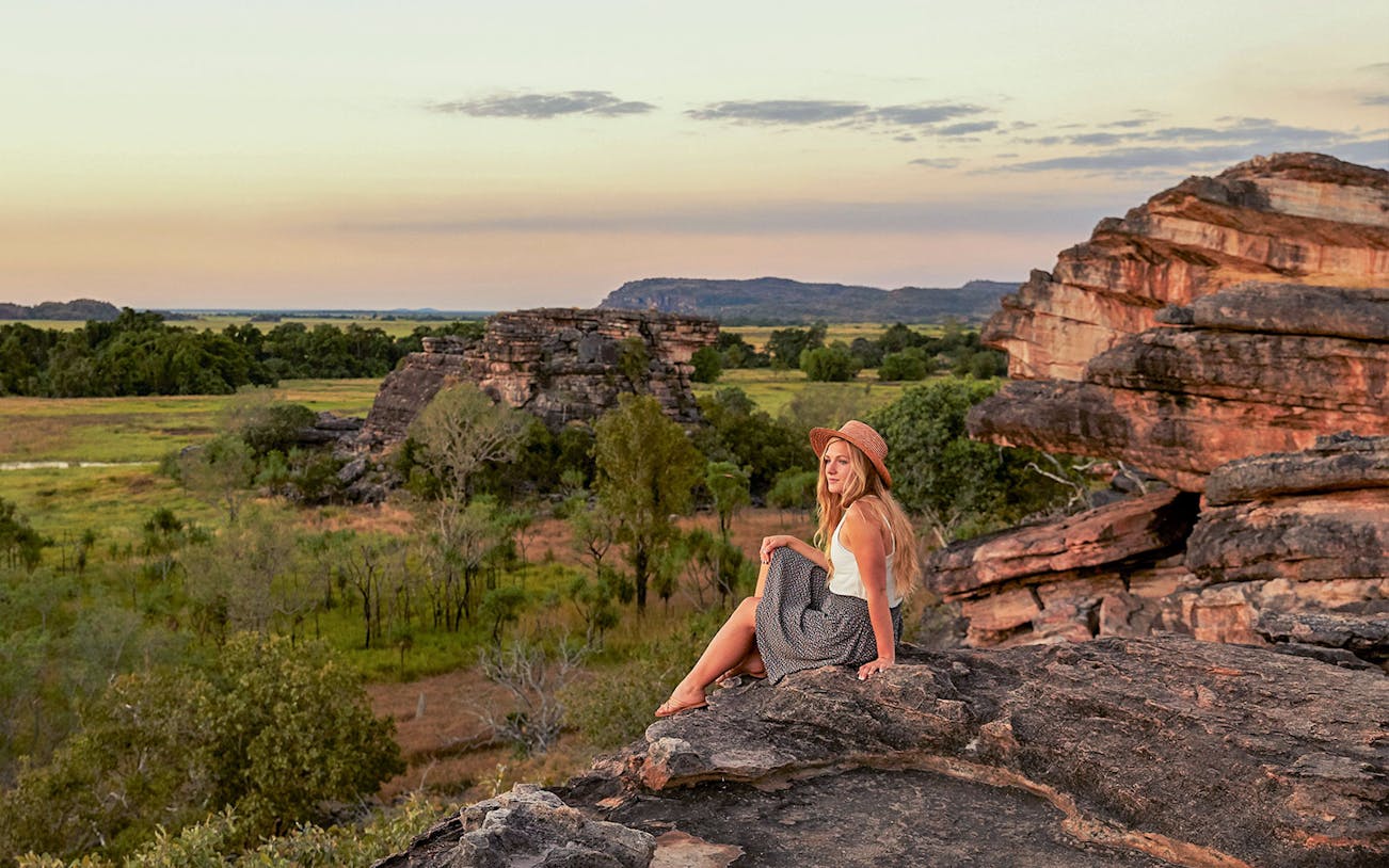 Woman sitting at Ubirr lookout with view of Kakadu National Park, Australia.