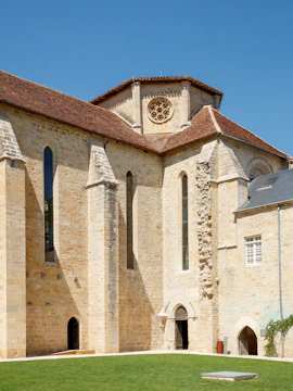 Beaulieu-en-Rouergue Abbey stone facade with arched windows and green lawn.