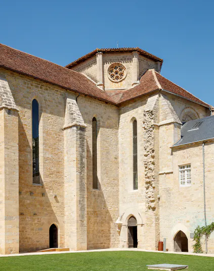 Beaulieu-en-Rouergue Abbey stone facade with arched windows and green lawn.