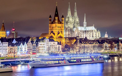 Cruise ship on the Rhine River with Cologne Cathedral illuminated at night.
