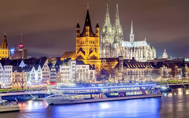 Cruise ship on the Rhine River with Cologne Cathedral illuminated at night.