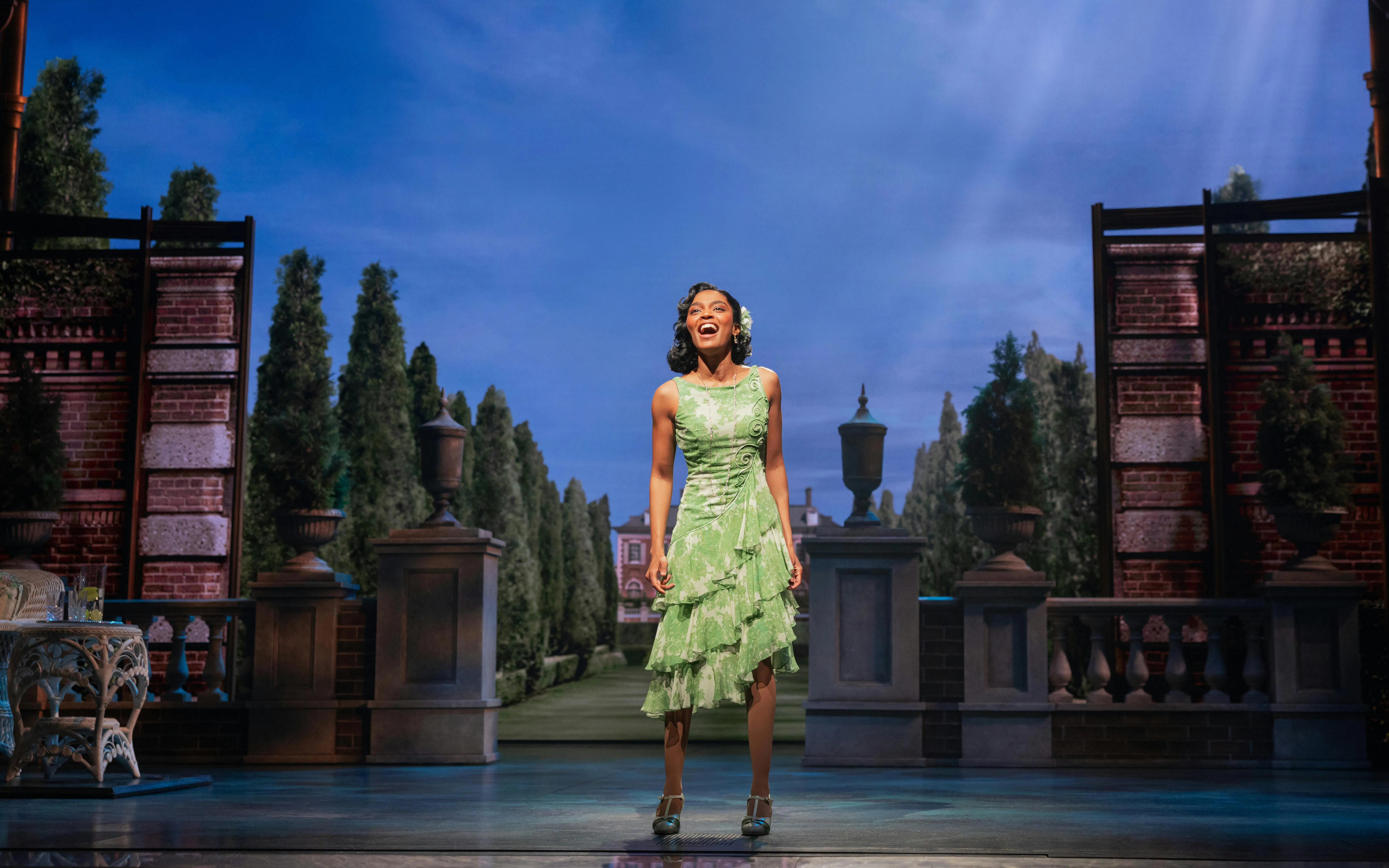 Performer on stage in The Great Gatsby musical, Broadway set with garden backdrop.